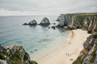 Vue panoramique d'une plage bretonne sauvage avec falaises rocheuses, sable doré et mer turquoise