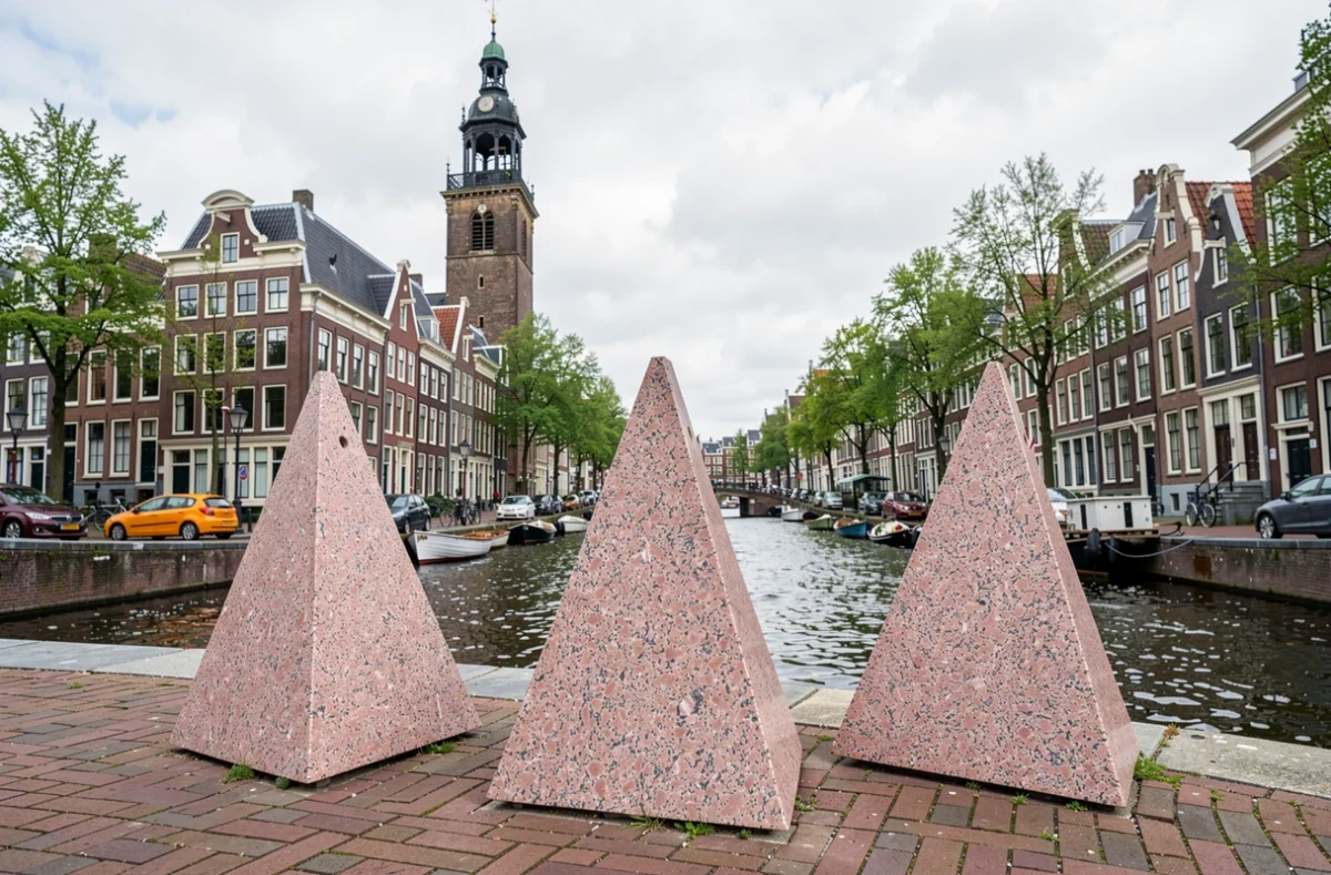 Monument aux trois triangles de granit rose au bord d'un canal d'Amsterdam